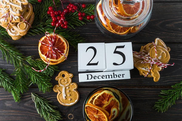 Calendario de madera con fecha 25 de diciembre, decoración navideña, galletas de jengibre, chips de naranja sobre fondo de madera — Foto de Stock