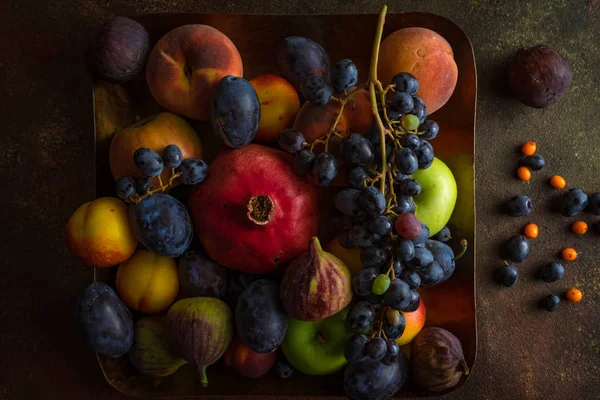 Berbagai buah-buahan berwarna-warni: delima, anggur, persik, plum, apel, ara di piring persegi — Stok Foto