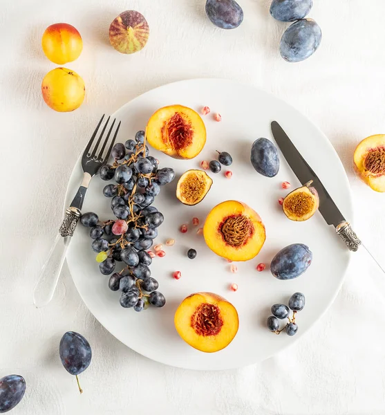Persikor, nektariner, vindruvor, fikon på vit plåt, bestick på vit bordsduk — Gratis stockfoto