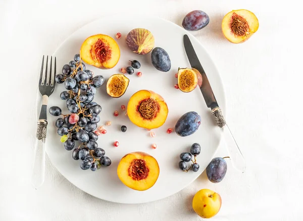 Persik setengah, nektarin, anggur, ara di piring putih, sendok makan di taplak meja putih, dengan ruang fotokopi — Stok Foto