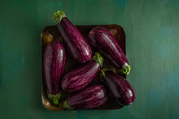 Gestreepte paarse aubergines in vierkante schotel op donker groene achtergrond. — Gratis stockfoto