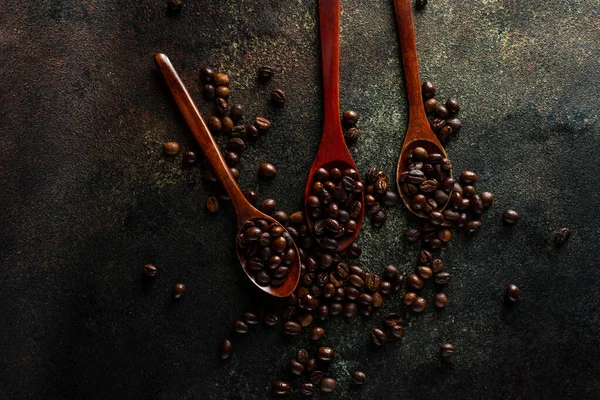 Drei Holzlöffel voll Kopi Luwak Kaffeebohnen auf dunklem Hintergrund — Stockfoto
