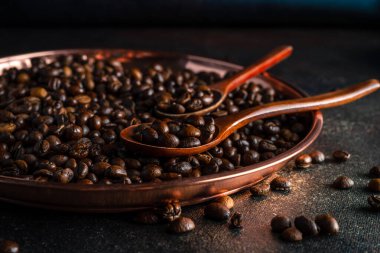 Yuvarlak bakır tepsi, arka planda iki kaşık dolusu kopi luwak kahve çekirdeği, yakın plan görüntüsü.