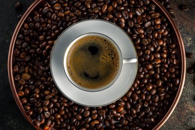 Yuvarlak bakır tepside kopi luwak kahve çekirdekleri, koyu fonda çay tabağı olan beyaz kahve, üst manzara, yakın çekim