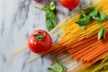 İtalyan makarnası pişirmek - çok renkli kuru makarna, taze domates, mermer tahtada fesleğen