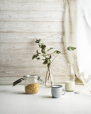 Granola, bir fincan süt ve vazoda çiçekler.