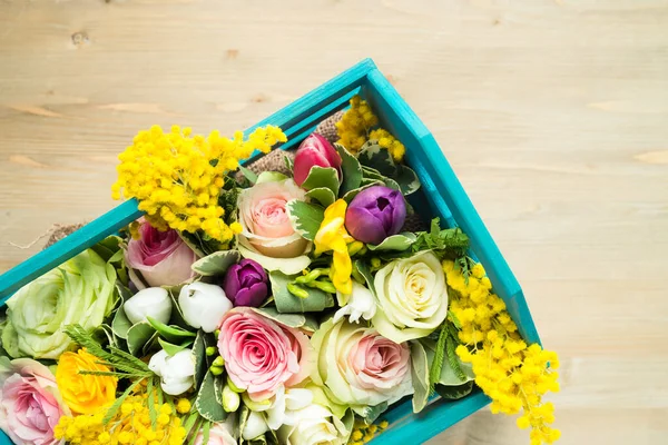 Top view of assorted flowers in a wooden box on a wooden background