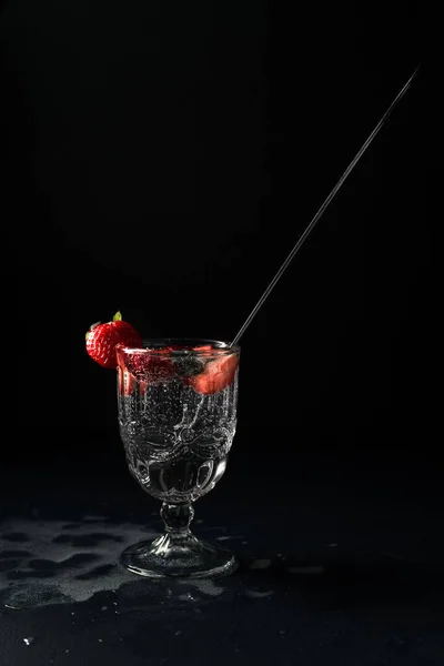 glass with cocktail and strawberries on black background