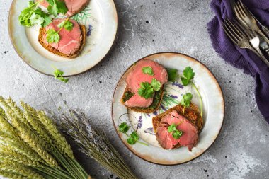 Etli sandviçler ve tabakta otlar.