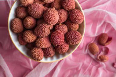 Pembe arka planda bir kasedeki liçi meyvelerinin yukarıdan görünüşü