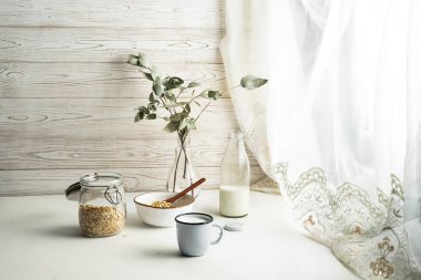 Granola, bir fincan süt ve vazoda çiçekler.