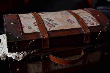 Ev dekorasyonunun bir parçası olarak koyu arkaplan üzerine masa örtüsü serili hafif açık bir eski tarz bagaj.