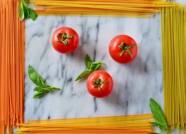 İtalyan makarnası pişirmek -- çok renkli kuru makarna, taze domates, mermer tahtadaki fesleğen, dikdörtgen bir çerçeve oluşturuyor