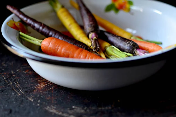 Multicolored carrots in white bowl on a dark background