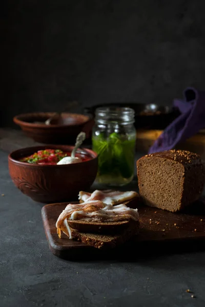 Traditional Russian meal of borscht soup, smoked bacon, and rye bread on a dark rustic background