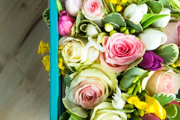 Top view of assorted flowers in a wooden box on a wooden background