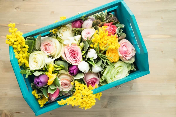 Top view of assorted flowers in a wooden box on a wooden background