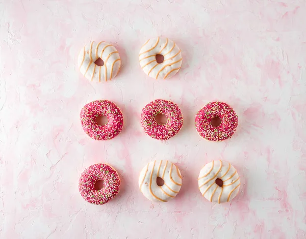 Assorted glazed doughnuts on a pink background