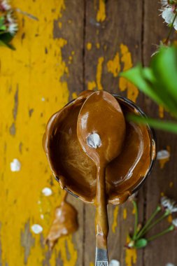 Bir bahar günü eski sarı bir bahçe masasında servis edilen bardaktaki son moda Kore dalgona kahvesi, üstünde krema dolu bir kaşık. Kopya alanı olan bir portre oryantasyonu. Üst görünüm