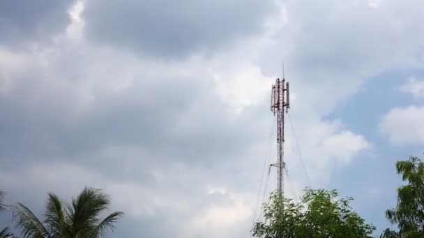 赤と白のネットワーク通信マストタワーは 木の頂上と深い青い熱帯の曇り空と時間が経過します ネットワーク放送塔 — ストック動画