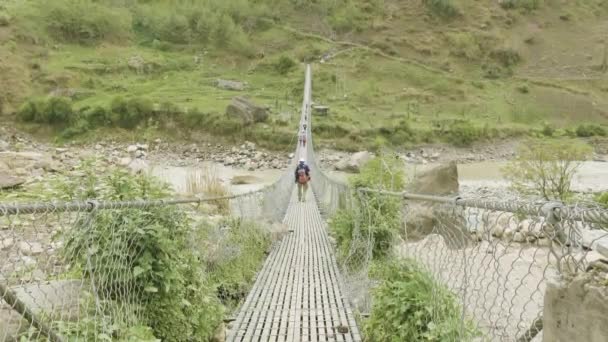 Backpackers ходити по підвісний міст над річкою в Непалі. Манаслу trek ланцюга. — стокове відео