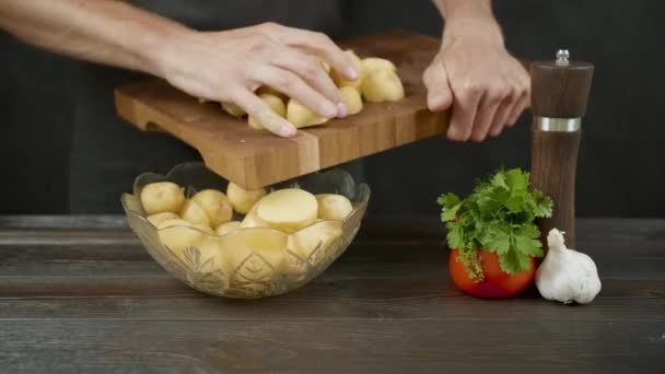 Człowiek umieścić ziemniaki z drewnianej deski do krojenia do miski w ciemnej kuchni — Wideo stockowe