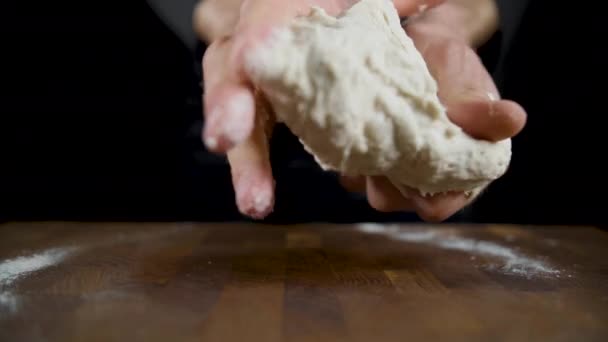 Кука викочується тісто на дерев'яному столі в темній кухні — стокове відео