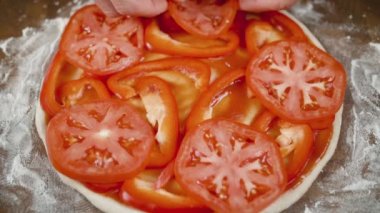 Bir adam pizza için hamurun üzerine domates serer, eller yukarı.