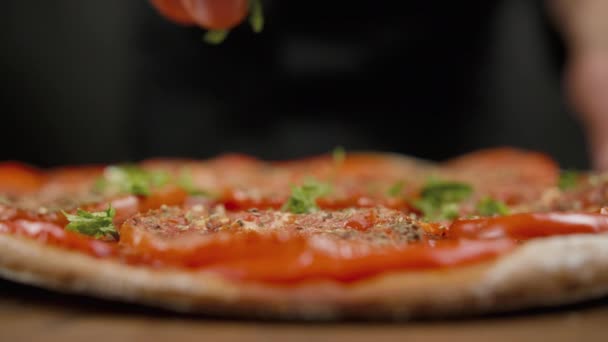 Шеф-повар разбрызгивает зеленью пиццу на черном фоне — стоковое видео