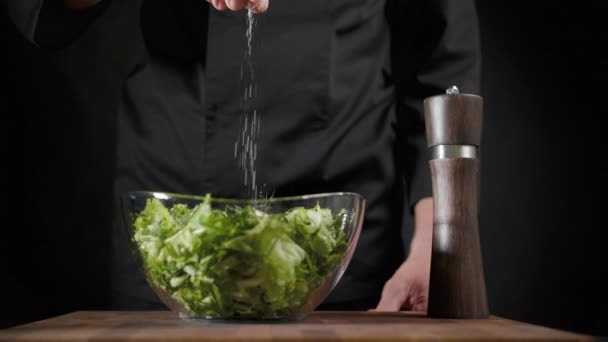 Cocine espolvorea sal y especias al salat verde sobre el fondo negro — Vídeos de Stock