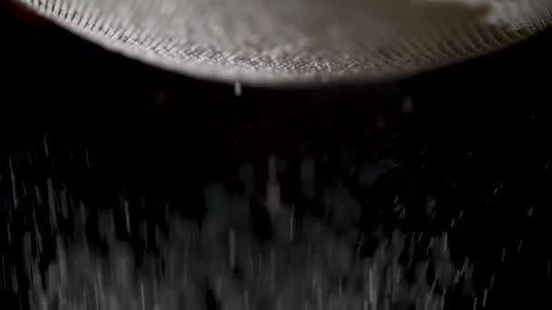 Flour is sifted through a sieve on black background — Stock Video