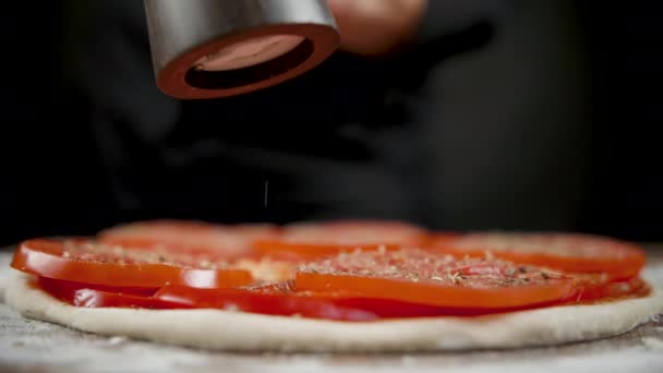 厨师在黑色背景上撒盐和香料给披萨 — 图库视频影像