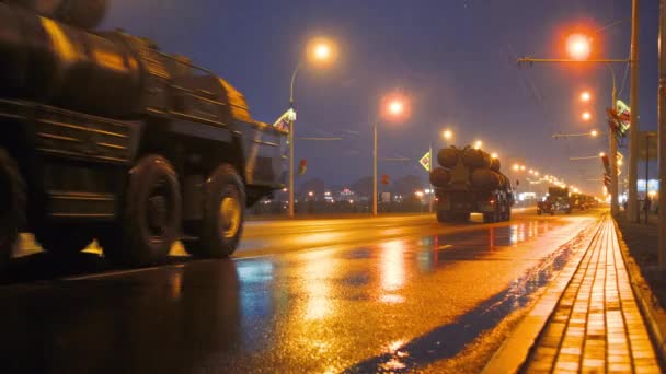 軍事機器の輸送隊は、ヘッドライトをオンにして夜に街を通って乗ります — ストック動画