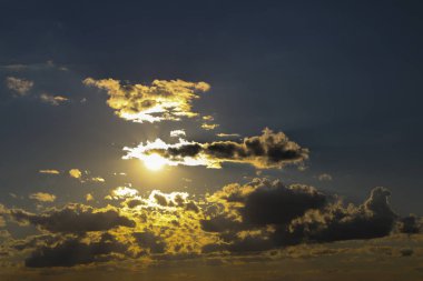 mavi gökyüzü beyaz bulutlar ile akşam. Güneş bulutların arkasına gizler. gün batımında güneş ışınlarının kabarık bulutlar farklı renk aydınlatmak.