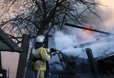 İtfaiye yangını söndürür. Ahşap yapı duman içinde yanan güçlü akış sulama hortumu su ile tutarak itfaiyeci.