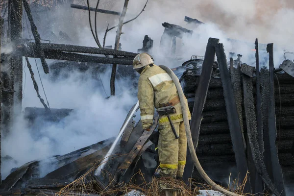 Firefighter extinguishes  fire. Fireman holding  hose with water, watering  strong stream of burning wooden structure in  smoke.