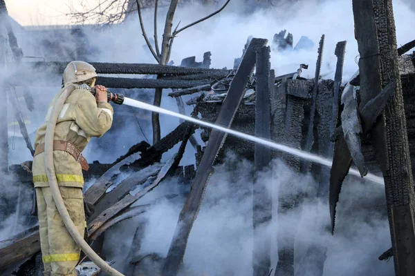 Firefighter extinguishes  fire. Fireman holding  hose with water, watering  strong stream of burning wooden structure in  smoke.