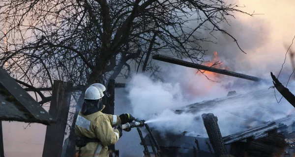 firefighter puts out  fire. firefighter in  smoke pours  burning building with water from  hose.