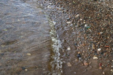 Deniz çakıl ve dalgalar. berrak su altındaki çakıl taşları ile kıyıya yakın. Dalgalar deniz kıyısında çökmesini ve sahil çakıl akan.