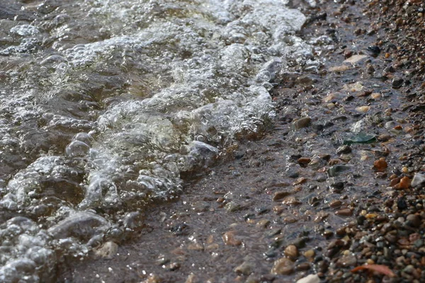 Havet småsten och vågor. klart vatten nära stranden med grus på botten. Havet vågor kraschar på stranden och flyter ovanför seashore pebble. — Stockfoto