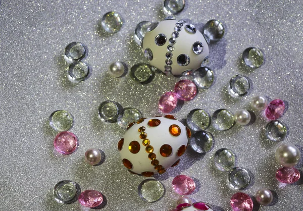 Easter composition flatlay. Easter eggs are decorated with shiny rhinestones on a silver background with glass ornaments and pearl beads.