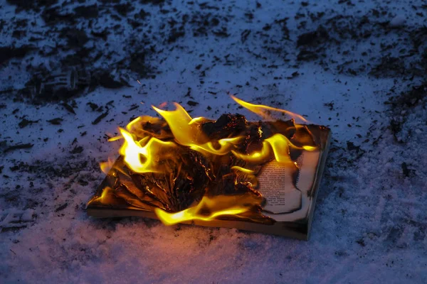 Livro em chamas na neve. páginas com o texto em livro aberto queimar com chama brilhante . — Fotografia de Stock
