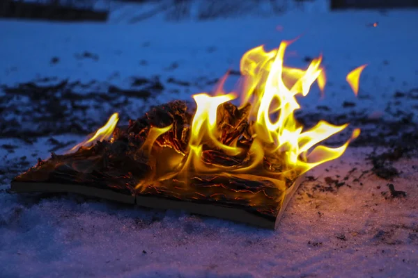 Livro em chamas na neve. páginas com o texto em livro aberto queimar wi — Fotografia de Stock