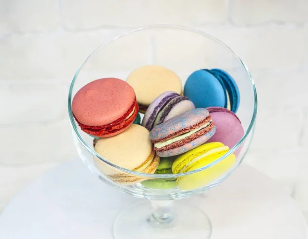 Bright colored and marbled macaroons in glass vase on white brick background. — Stock Photo, Image