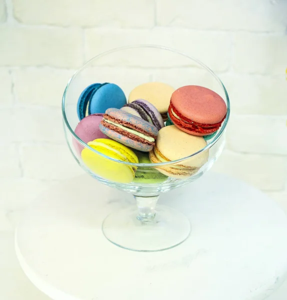 Bright colored and marbled macaroons in glass vase on white brick background. — Stock Photo, Image