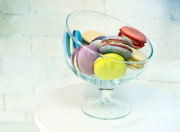 Bright colored and marbled macaroons in glass vase on white brick background. — Stock Photo, Image