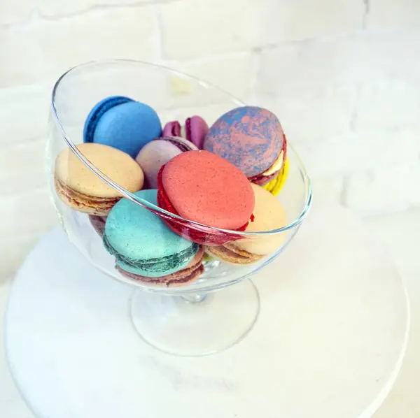 Bright colored and marbled macaroons in glass vase on white brick background. — Stock Photo, Image