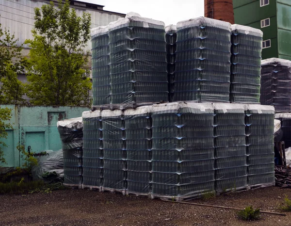 Fertige Produkte aus sauberen Flaschen werden in Paletten verpackt. Regale mit Flaschen stehen auf verlassenem Gelände nahe Glasfabrik in Waldnähe. — Stockfoto