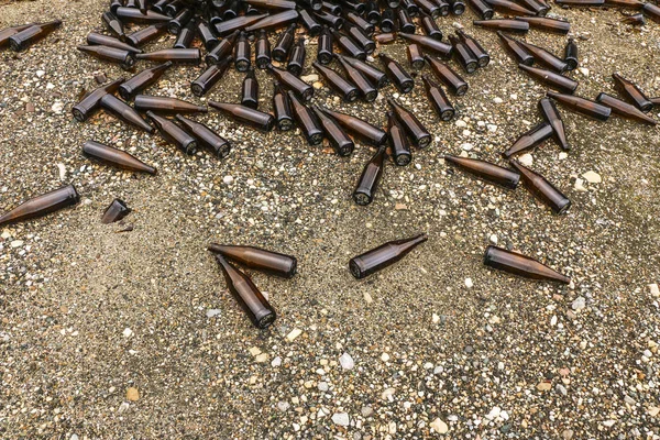 Garrafas marrons inteiras e quebradas estão espalhadas em cascalho.Conceito: reciclagem de resíduos, descarte de lixo — Fotografia de Stock