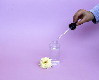 Yağ veya serum ile pipet ile cam şişe, hassas arka planda beyaz gül çiçeği ile. Konsept: organik biyo kozmetik, bitkisel yağlar, serum kollajen, Cilt Bakımı